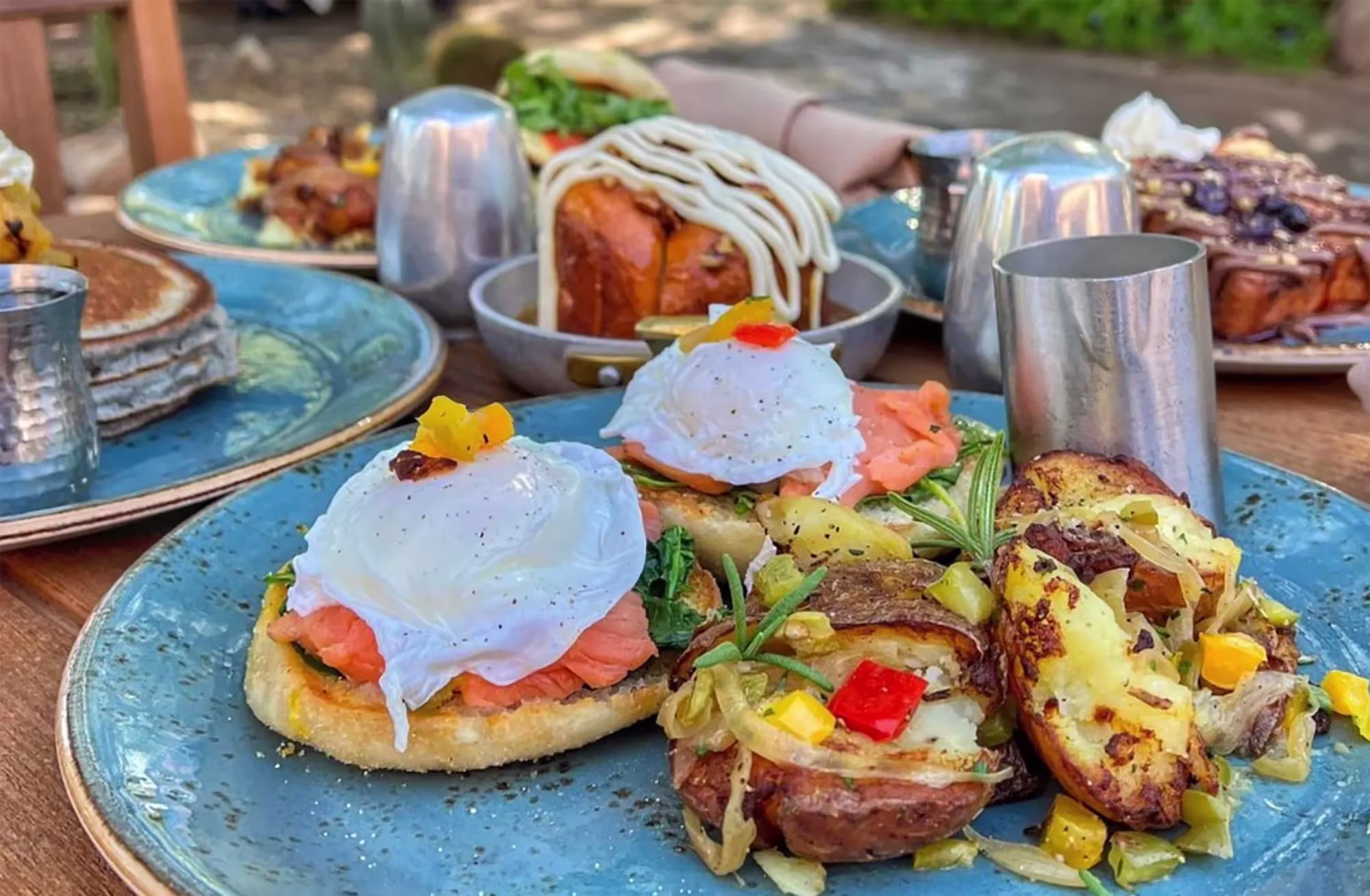 Plate with two poached eggs on smoked salmon and toasted English muffins, served with roasted potatoes topped with diced vegetables and herbs.